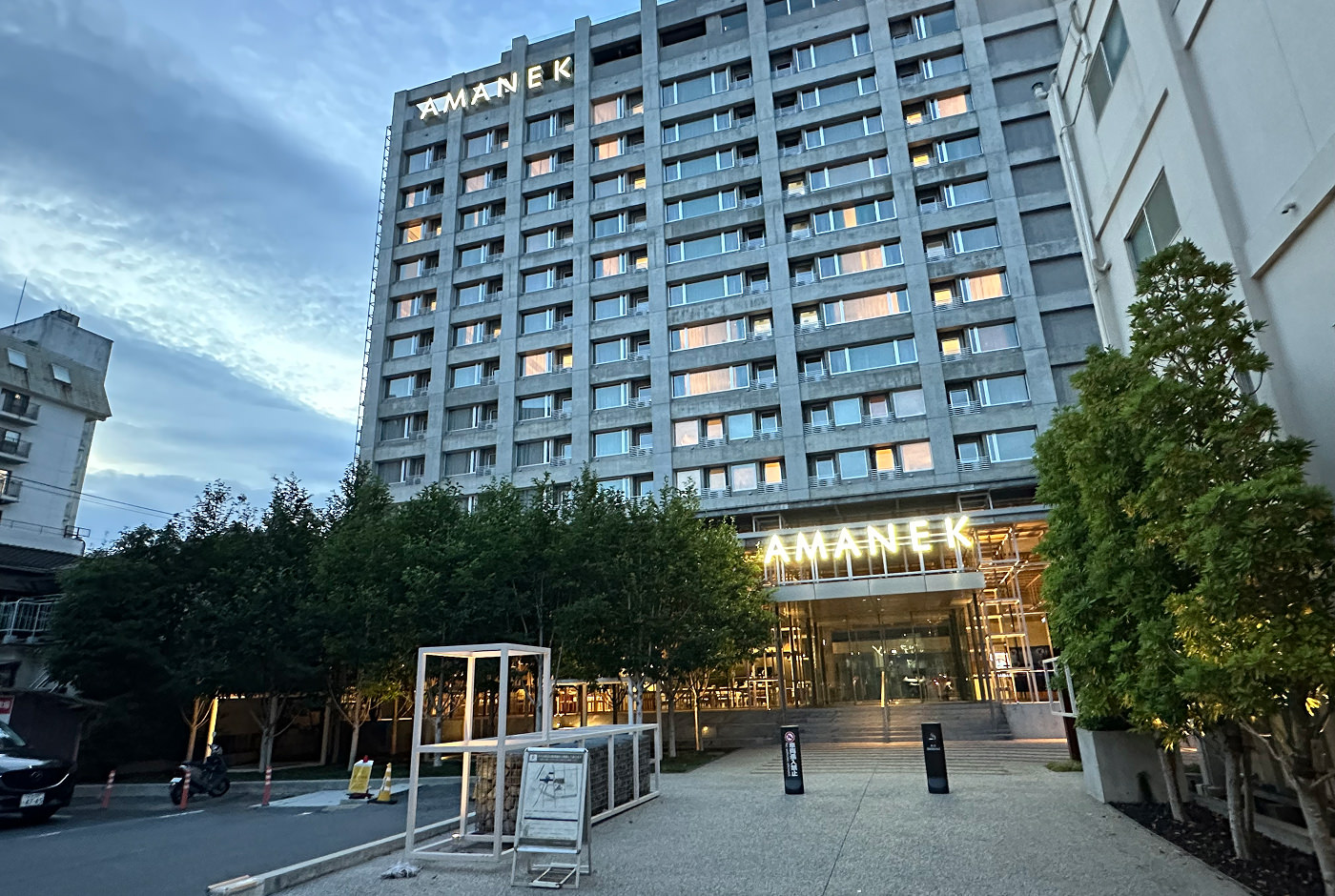 Fasaden på ett grått hotell med 14 våningar. Två gula skyltar lyder "Amanek".
