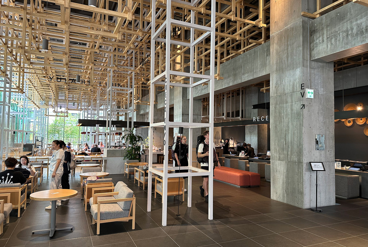 Ljus hotellobby med mörkt golv. I taket bildar träpinnar kubliknande mönster.