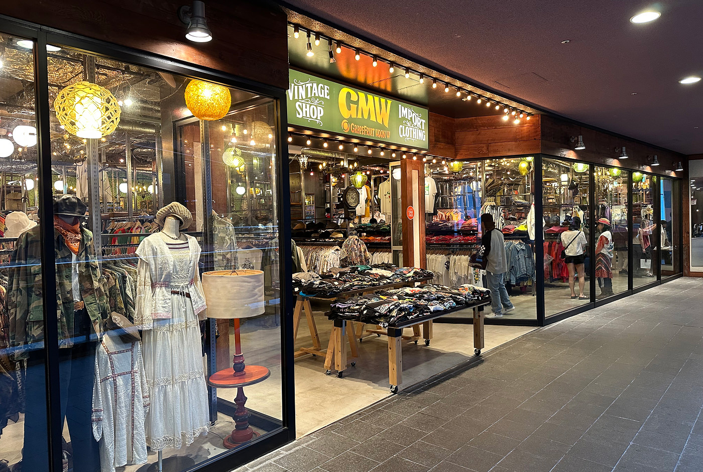 Upplyst glasfasad för en butik som säljer vintage-kläder. En grön skylt lyder "GMW Grapefruit Moon".