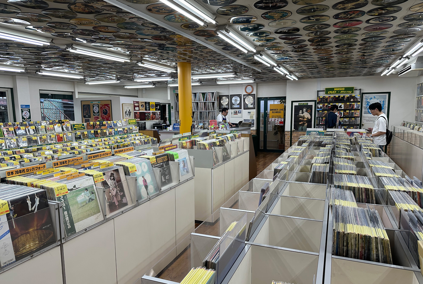 En stor och ljus skivbutik med massor av lådor fyllda med vinylskivor. Längs bort står en