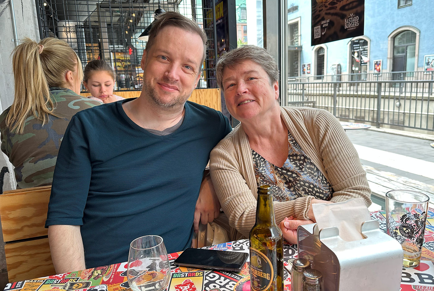 Dan och hans mamma sitter vid ett färgglatt matbord på en restaurang. De ler båda in i kameran.