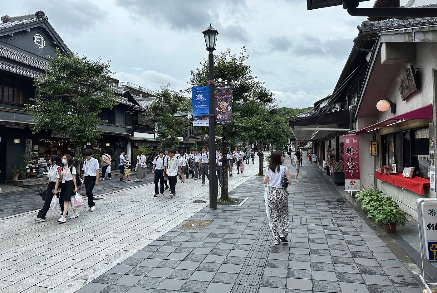 En bred och fin stengång mellan traditionella japanska hus. I husen finns det butiker och matställen. I mitten går många skolungdomar med vita skjortor.