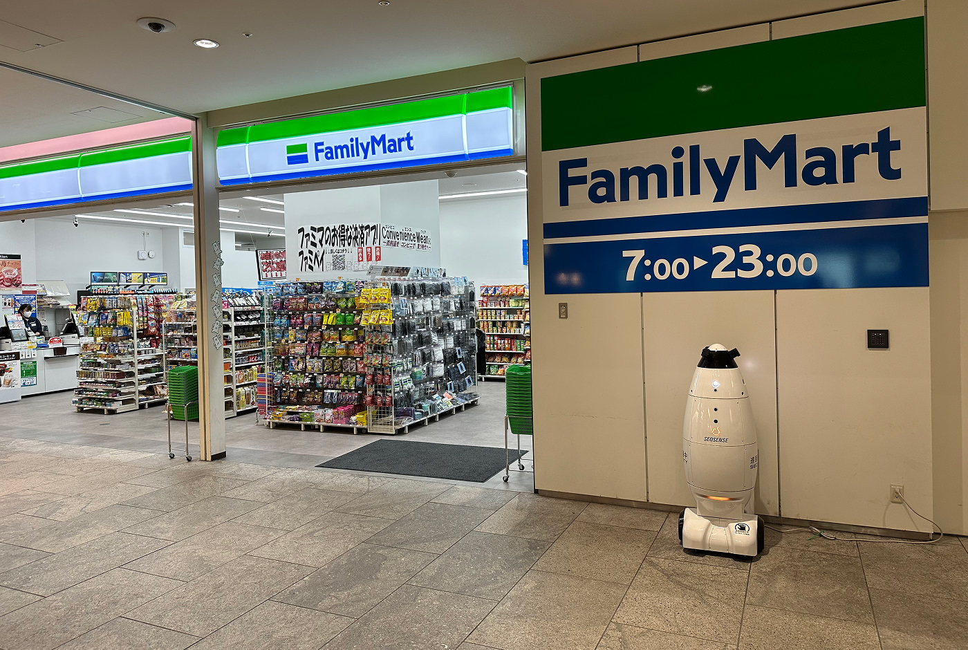 Ett litet snabbköp med stora dörrar och flera hyllor med olika färggranna påsar. En skylt lyder "FamilyMart".