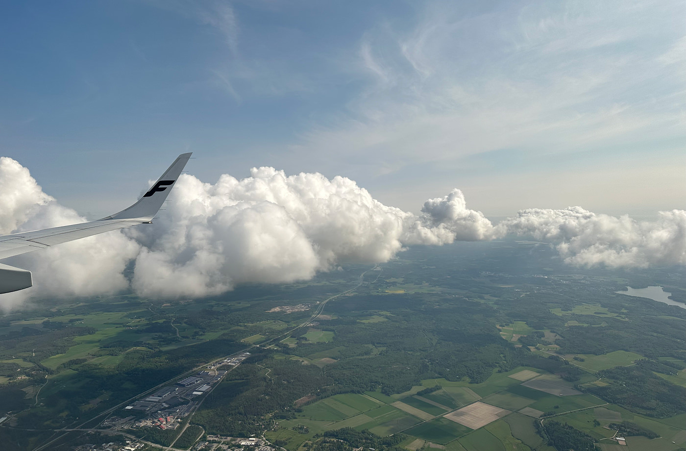 Utsikt över lummiga Helingsfors från ett flygplansfönster. Till vänster ser man flygplanets vinge.