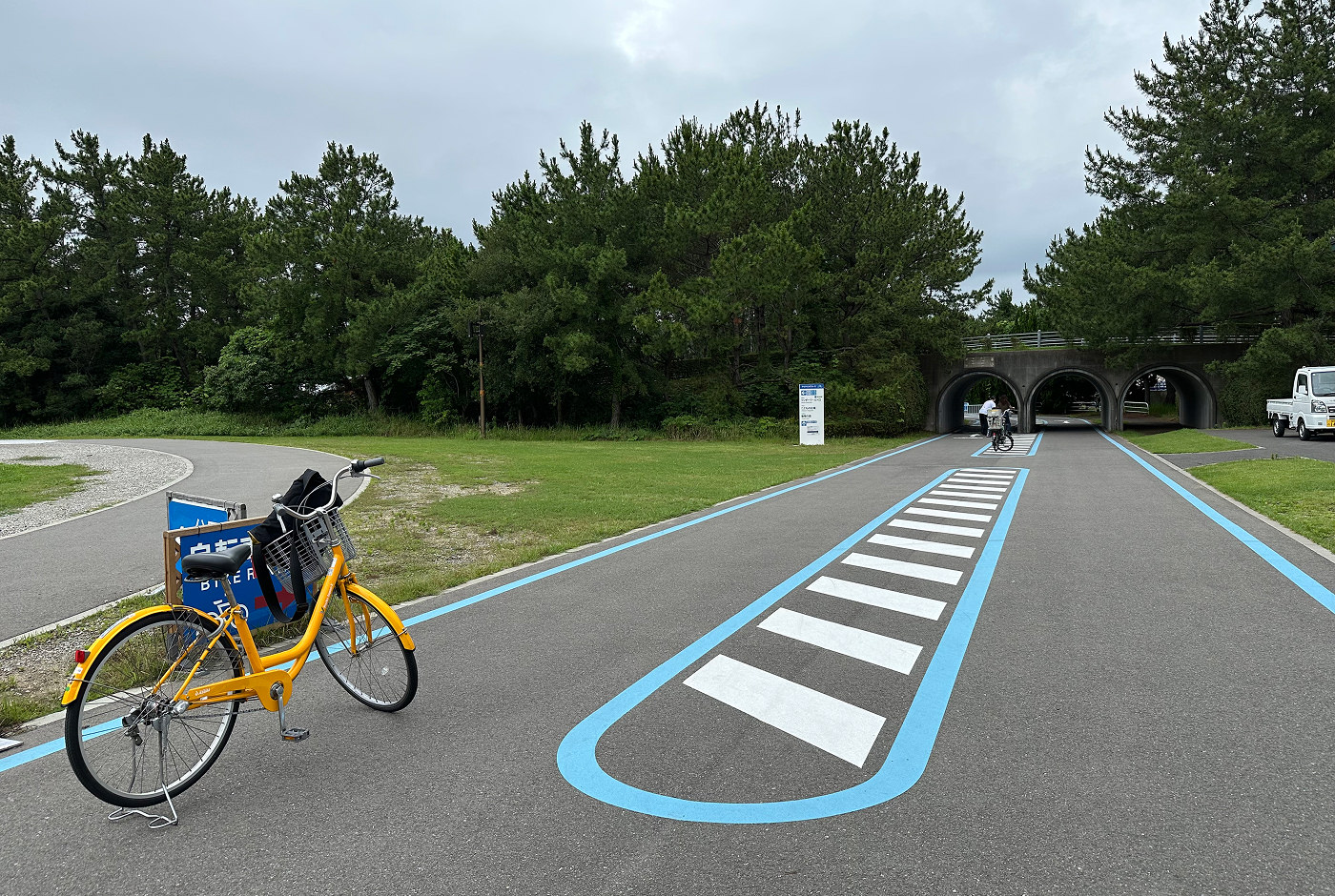 Gul cykel står parkerad på en tvåfilig cykelväg som går in i en park.