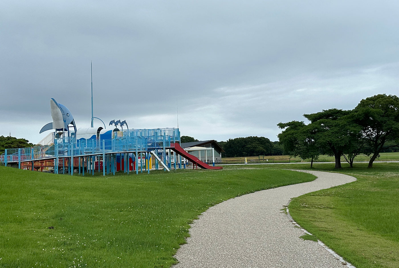 Klätterställning med en staty på en delfin omgiven av en park med välansad gräsmatta och buskiga träd.