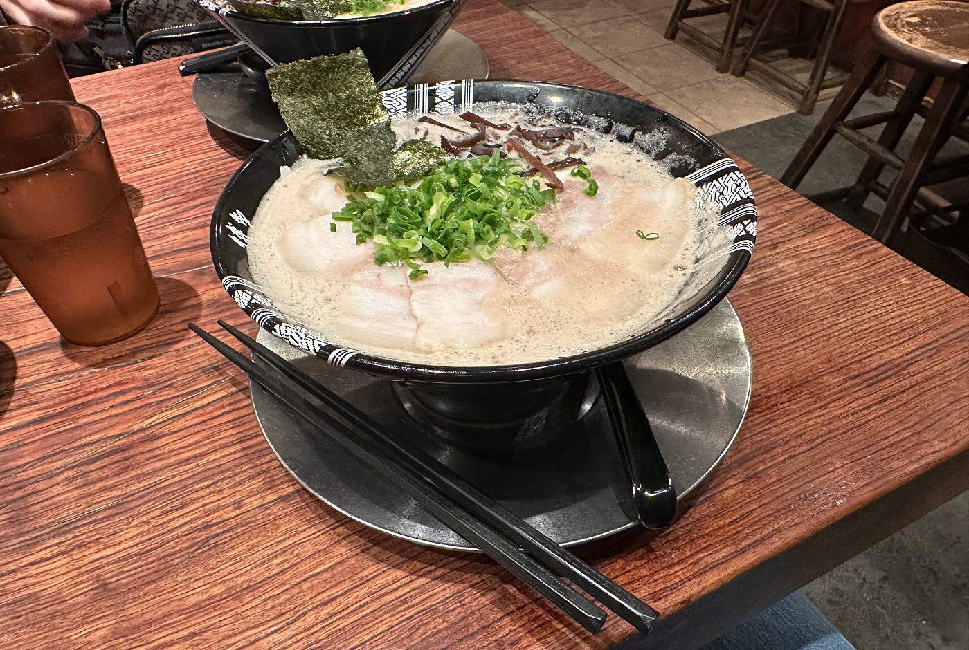 Svart skål med ramen med ljus sås garnerad med fläskkött, sjögräs och gräslök.
