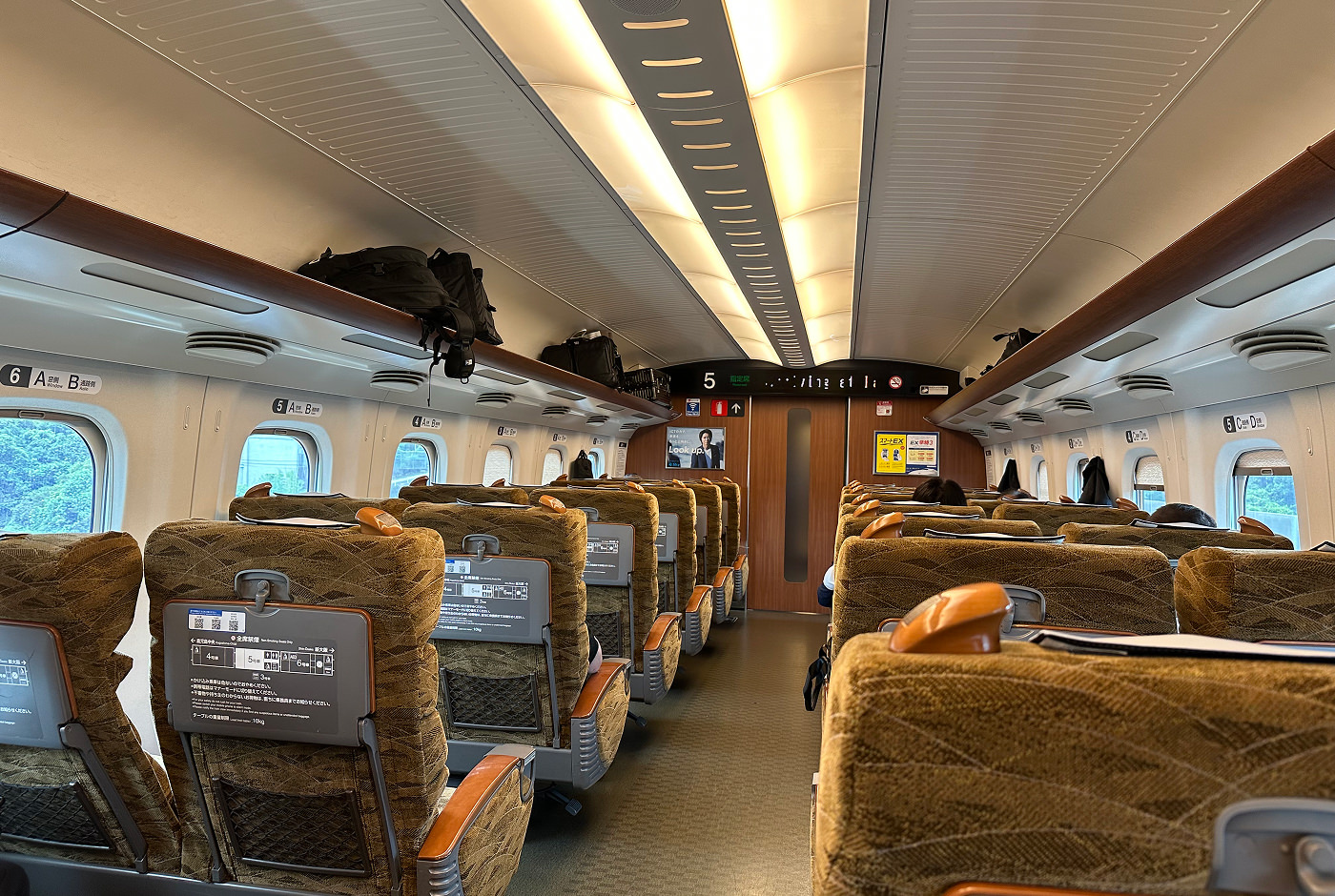 Inuti en tågvagn på Shinkansen. Sätena har brungult mönster. De flesta platser är lediga.
