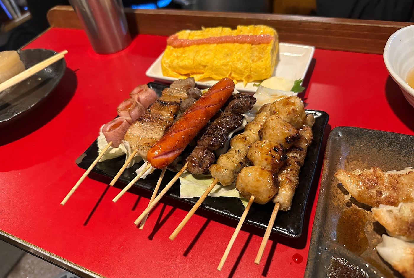 Röd bardisk med flera små brickor med mat. En har grillspett, en dumplingar och en äggomeletter.