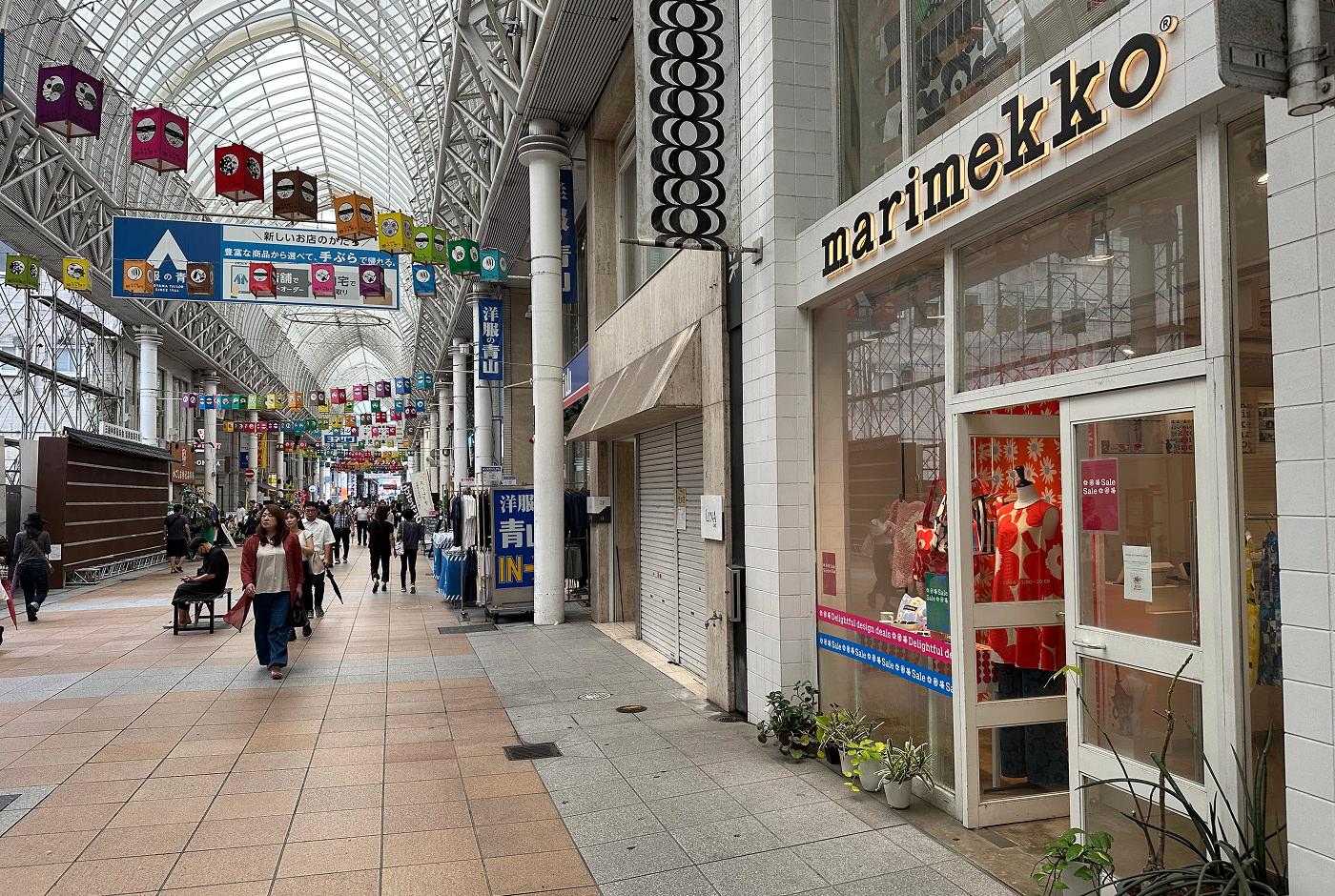 Lång shoppingarkad med ett högt, ljust och runt tak. Till höger finns en liten butik med skylten "Marimekko" som har färggranna kläder i skyltfönstret.