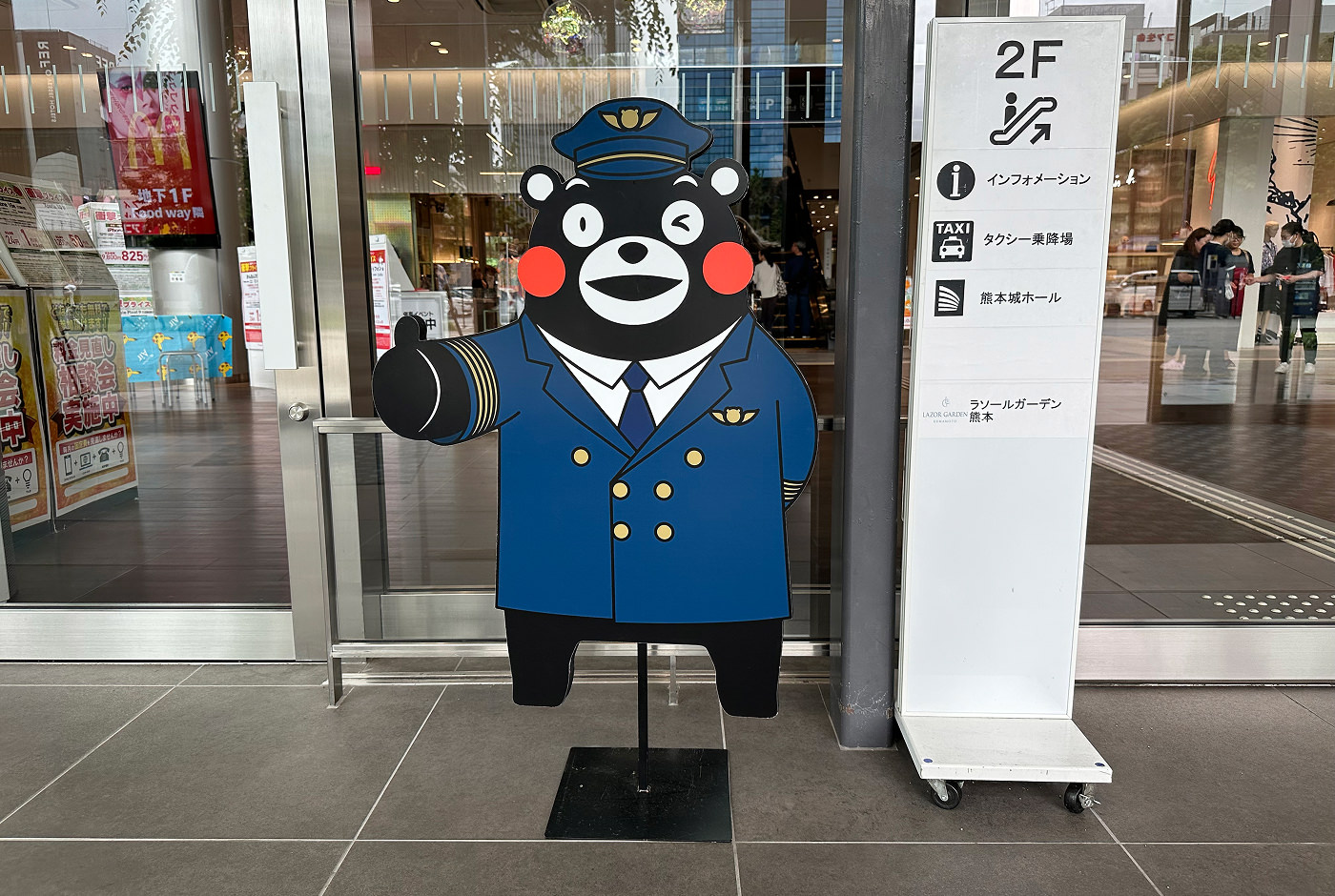 Det glada björnmonstret Kumamon är utklädd till en tågkonduktör och står vid ingången till en food court.