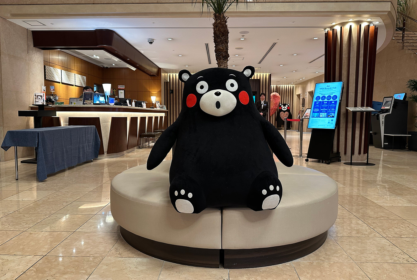 Den svarta glada björnen Kumamon sitter på en soffa i en hotellobby.