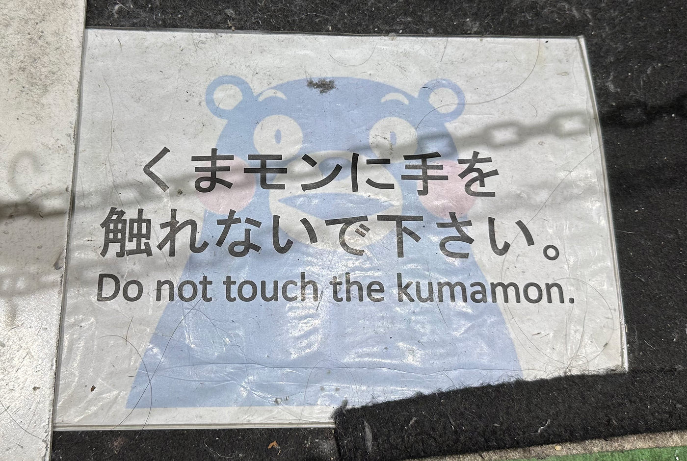 Varningsskylt på marken med text på japanska och engelska som lyder "Do not touch the kumamon".