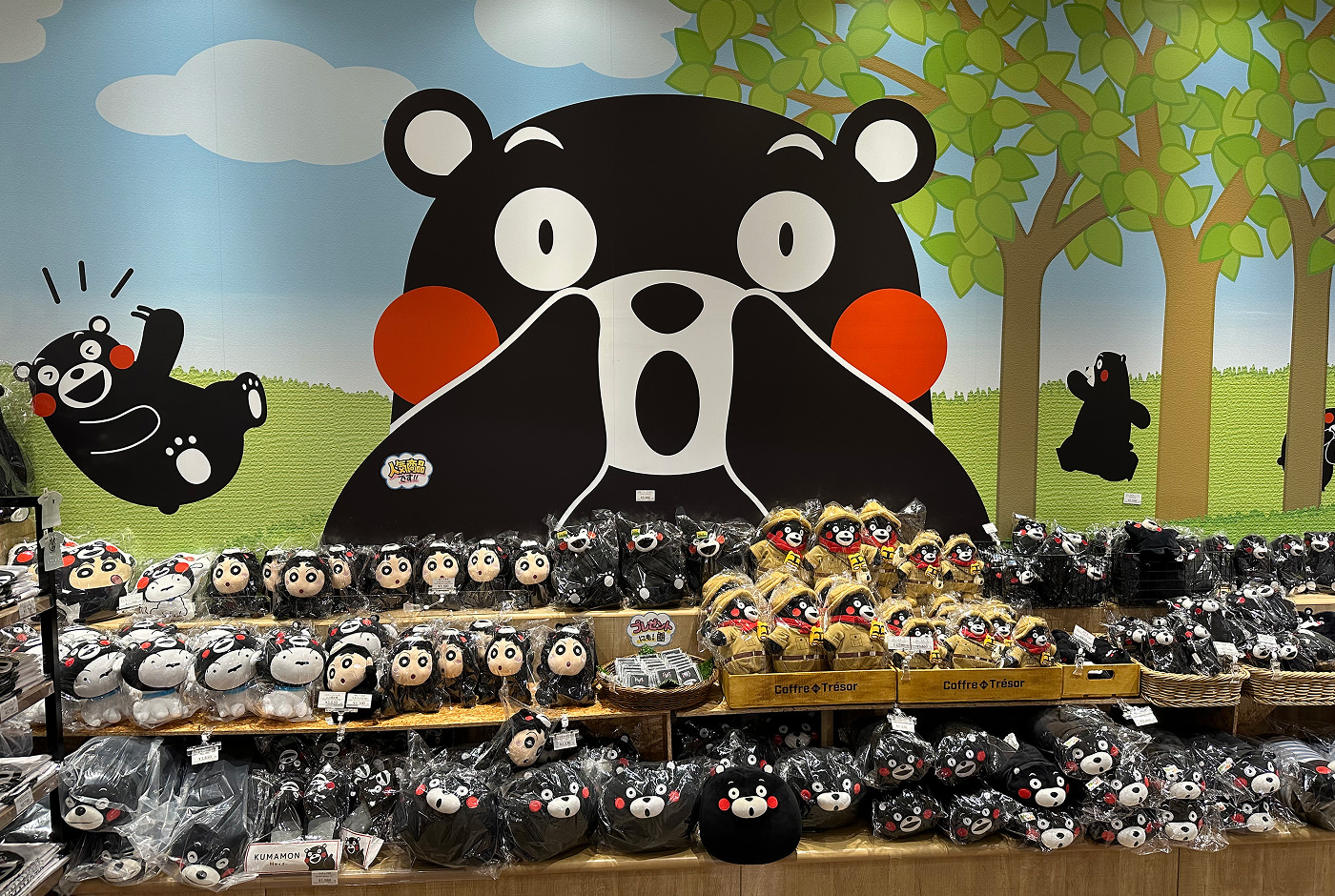 Stor väggmålning av den svarta glada björnen Kumamon bakom tre rador med kramdjur inslagna i plast.