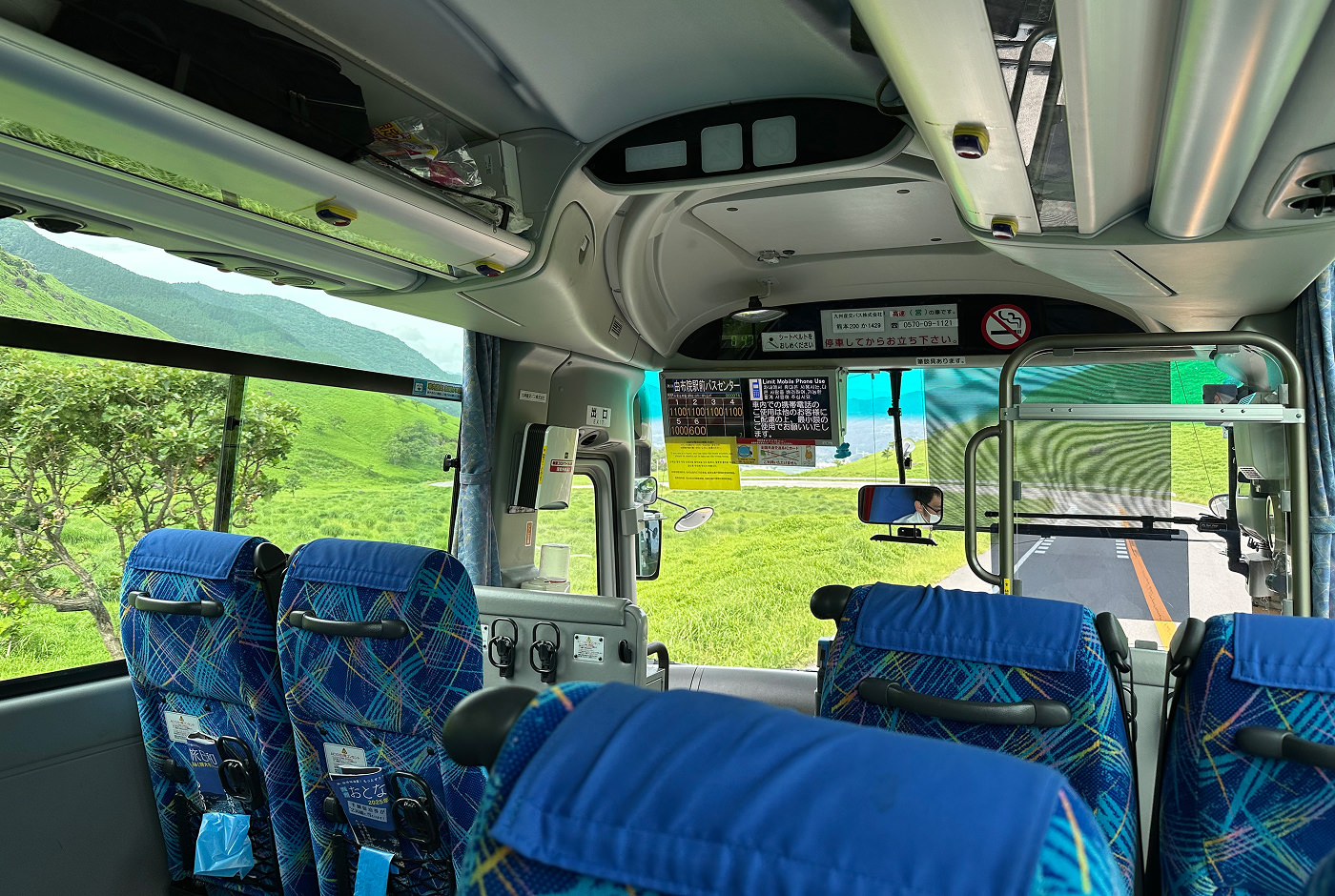 Inuti en buss med blå säten som åker nedför en lummig stor bergsdal.