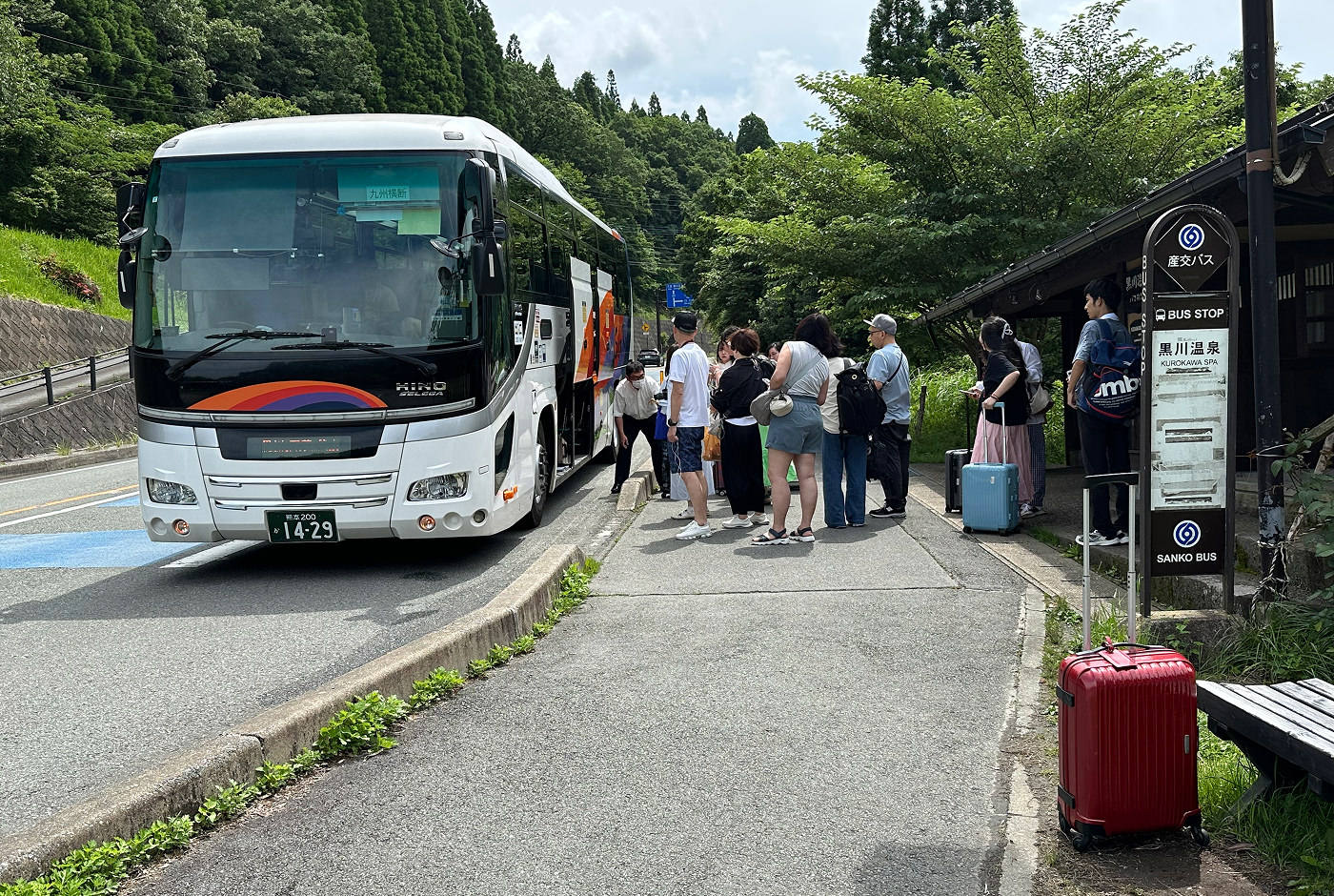 Ett tiotal personer står vid en buss vid en lummig landsväg och ska kliva på.