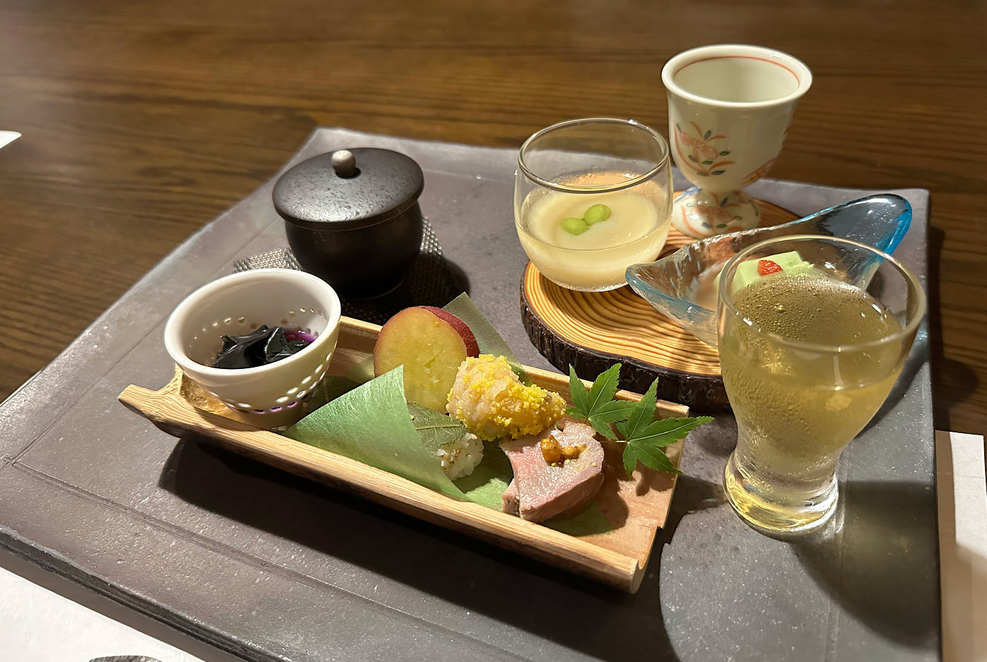 Ett glas med sake och sex små koppar med smårätter på en bricka.