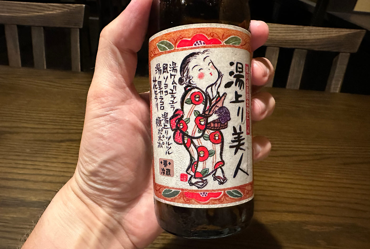 Hand håller i en ölflaska med en karikatyr på en geisha som håller i en skål.