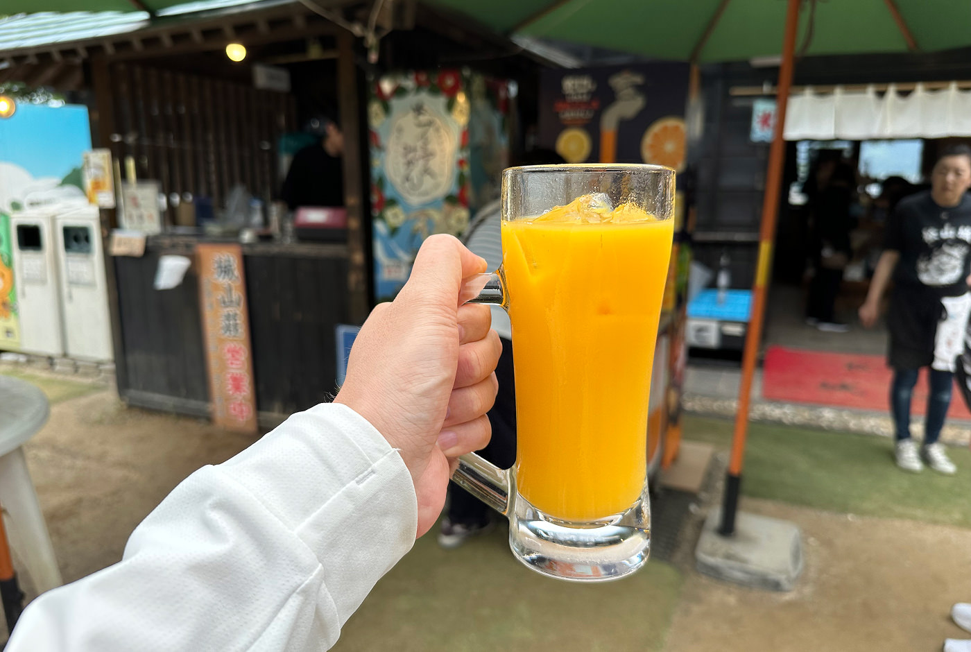 Min hand håller i ett stop med apelsinjuice med isbitar i.
