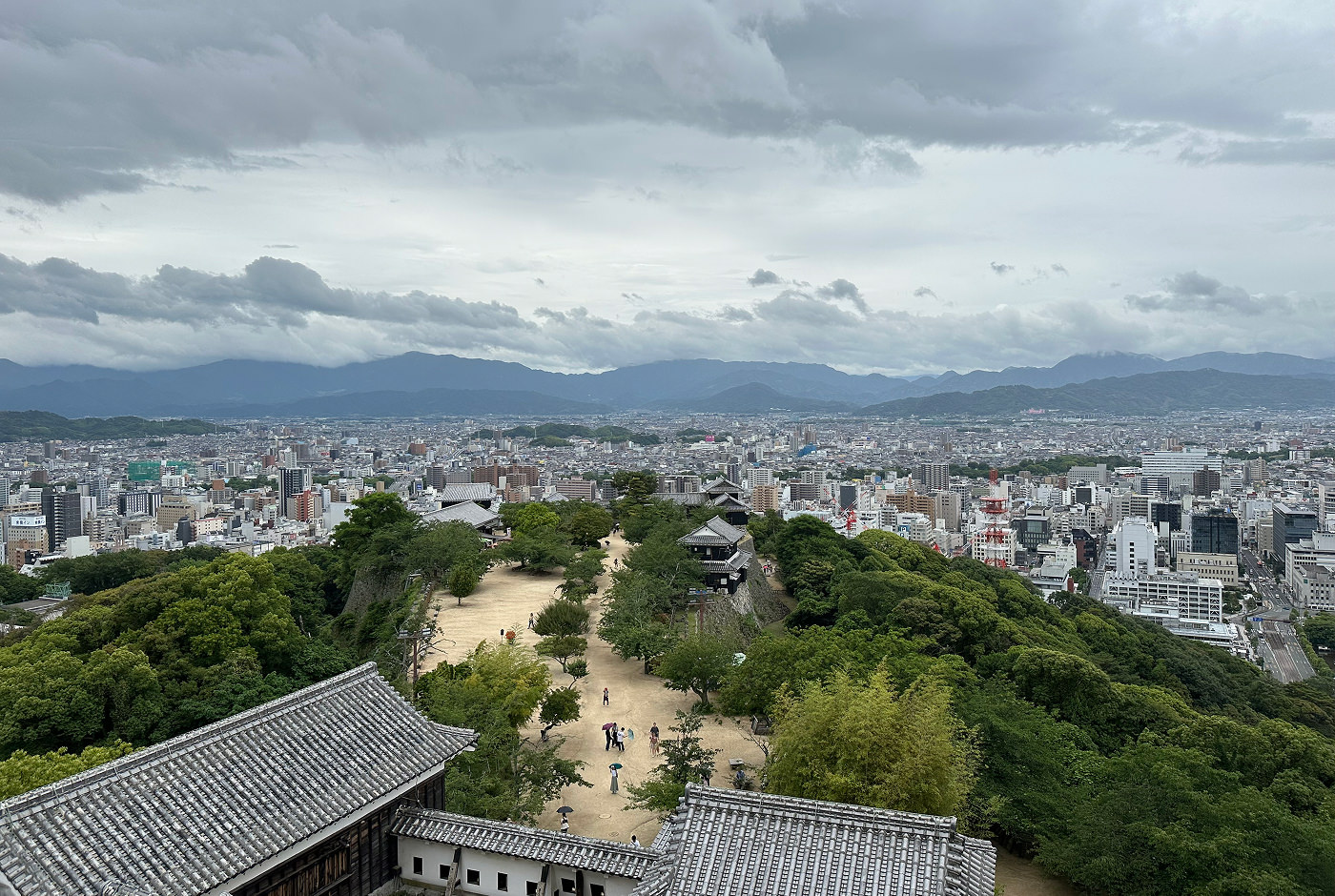 Utsikt över Matsuyama från en terass på ett slott. Nedan syns slottsgården med sitt ljusa grus och lummiga träd.