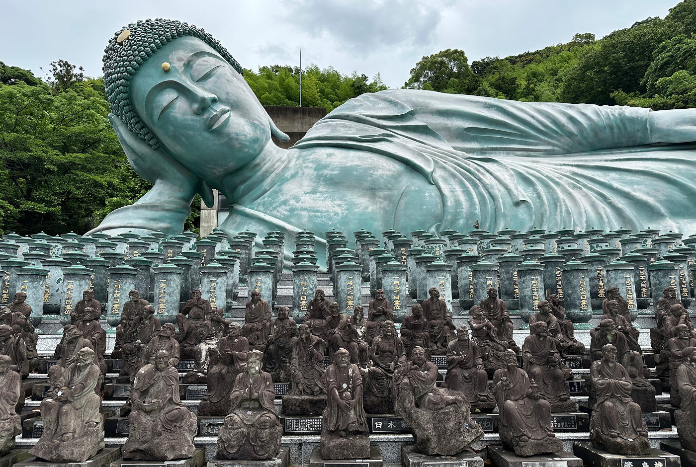 Detaljerade och humoristiska stenfigurer av buddhistiska munkar framför en enorm staty av en liggande buddha.