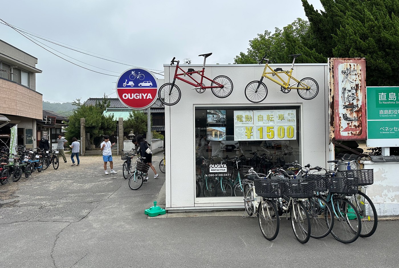 Ljus liten butiken cyklar utanför. En rund skylt har texten "Ougiya".
