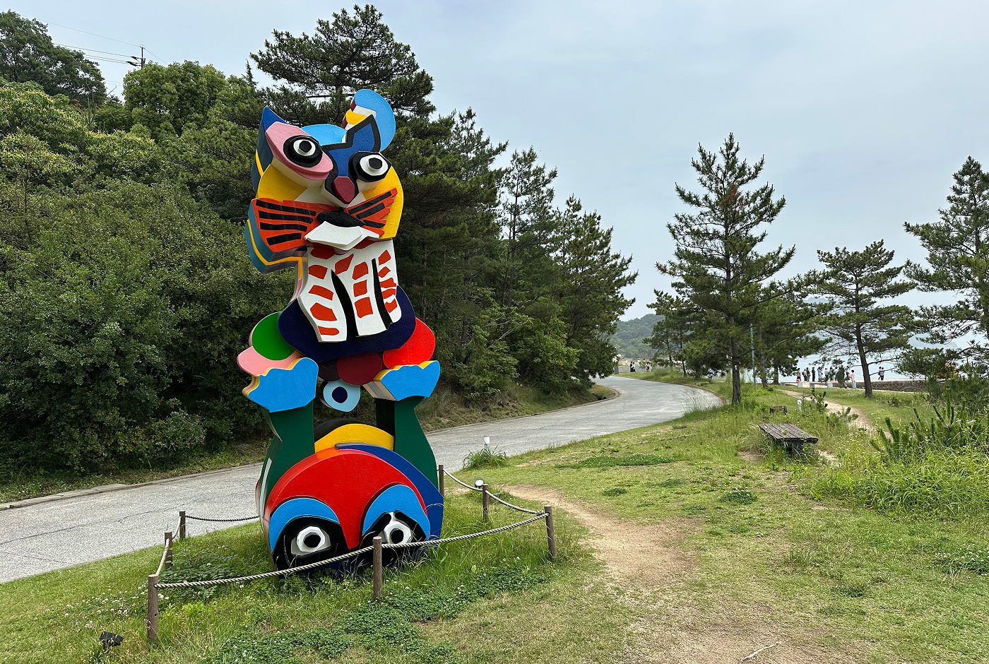 Drygt tre meter hög, färggran och surrealistisk staty av en groda och en katt i en lummig park.