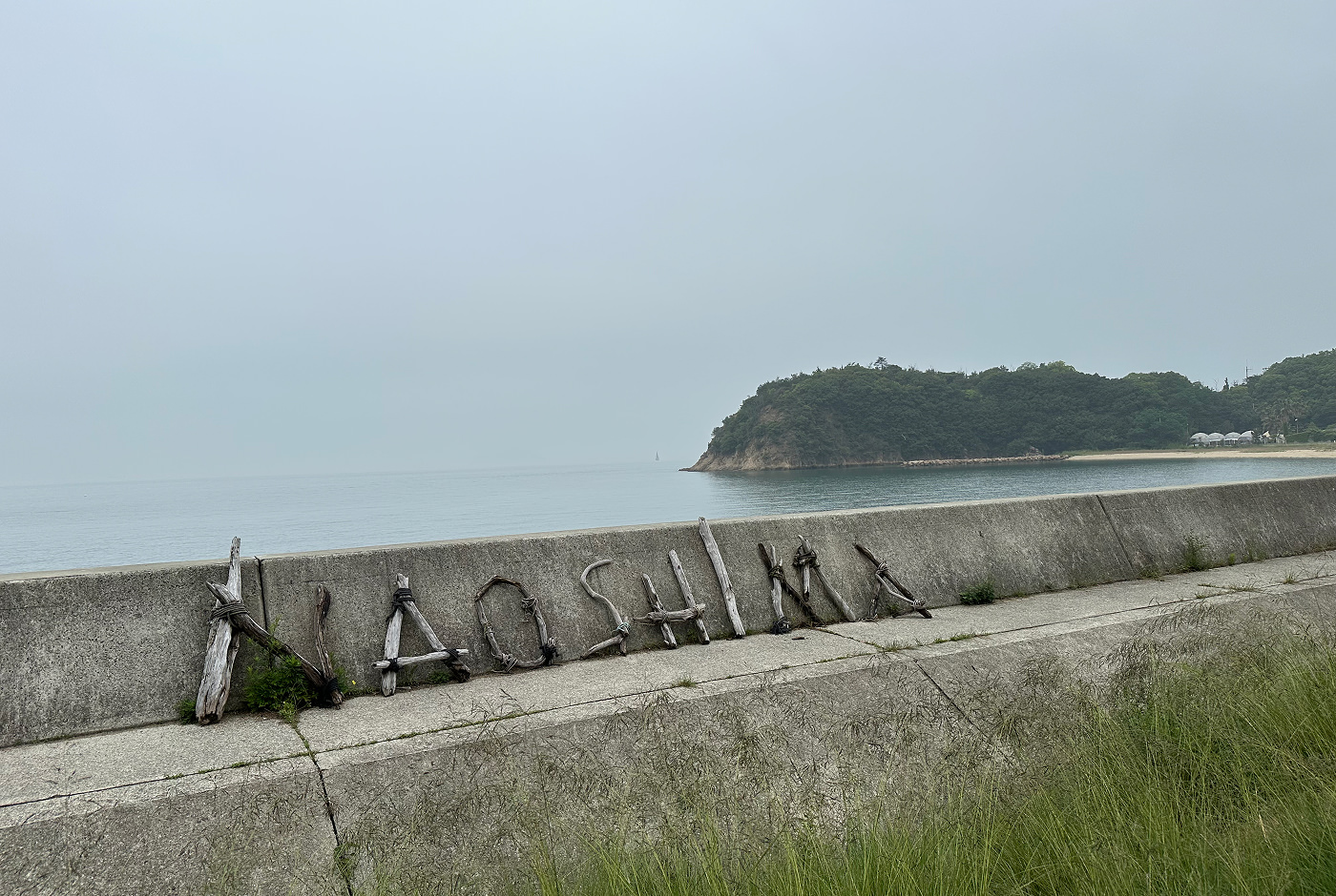 Sektion av en strand med en kraftig vågbytare. Bundna kvistar på den formar namnet "Naoshima".