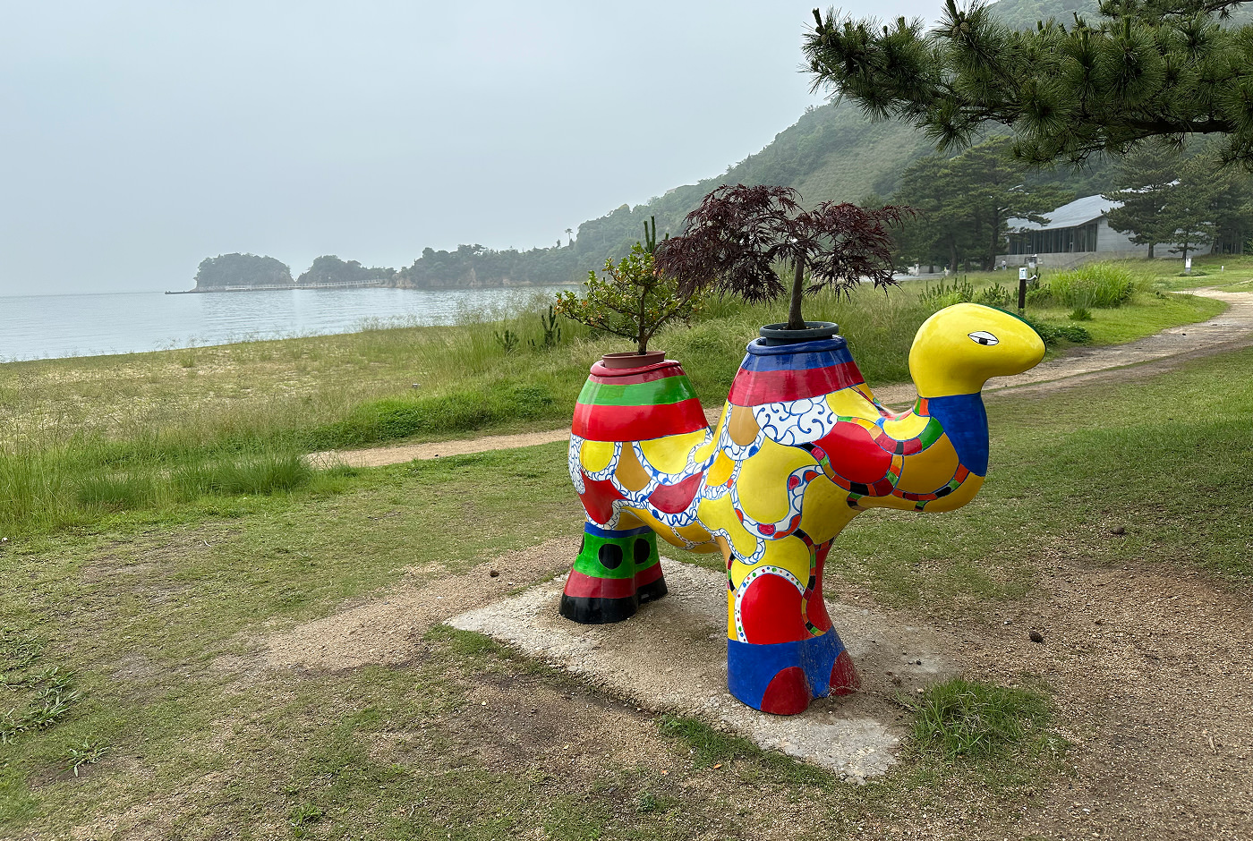 Lekfullt färggrann skulptur av en kamel på en gräsplätt vid en gång vid en strand.