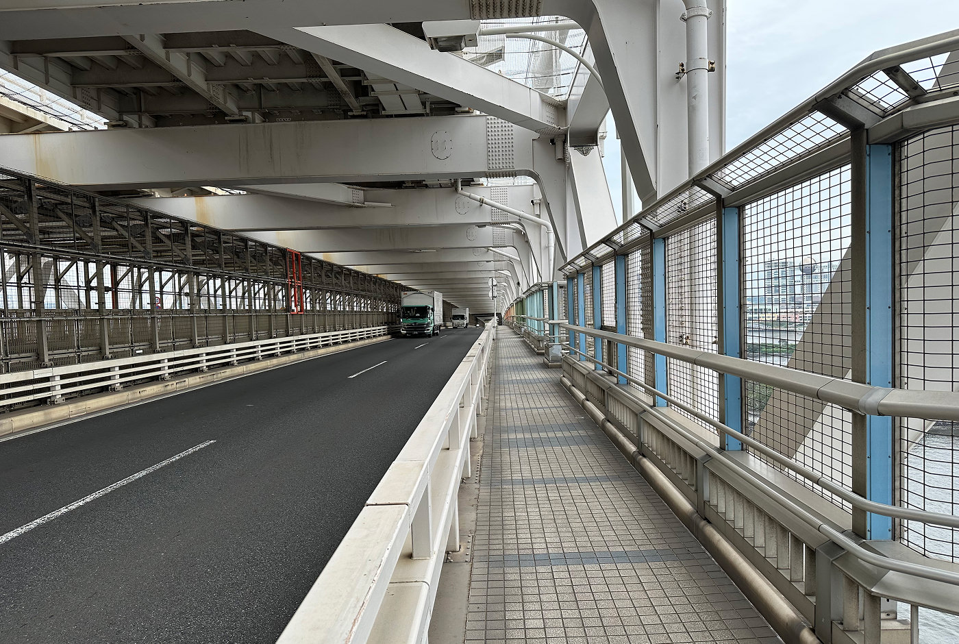 Inuti en enorm bro där bilar och monorail kör i mitten en trottoar finns till höger separerad av ett räcke.