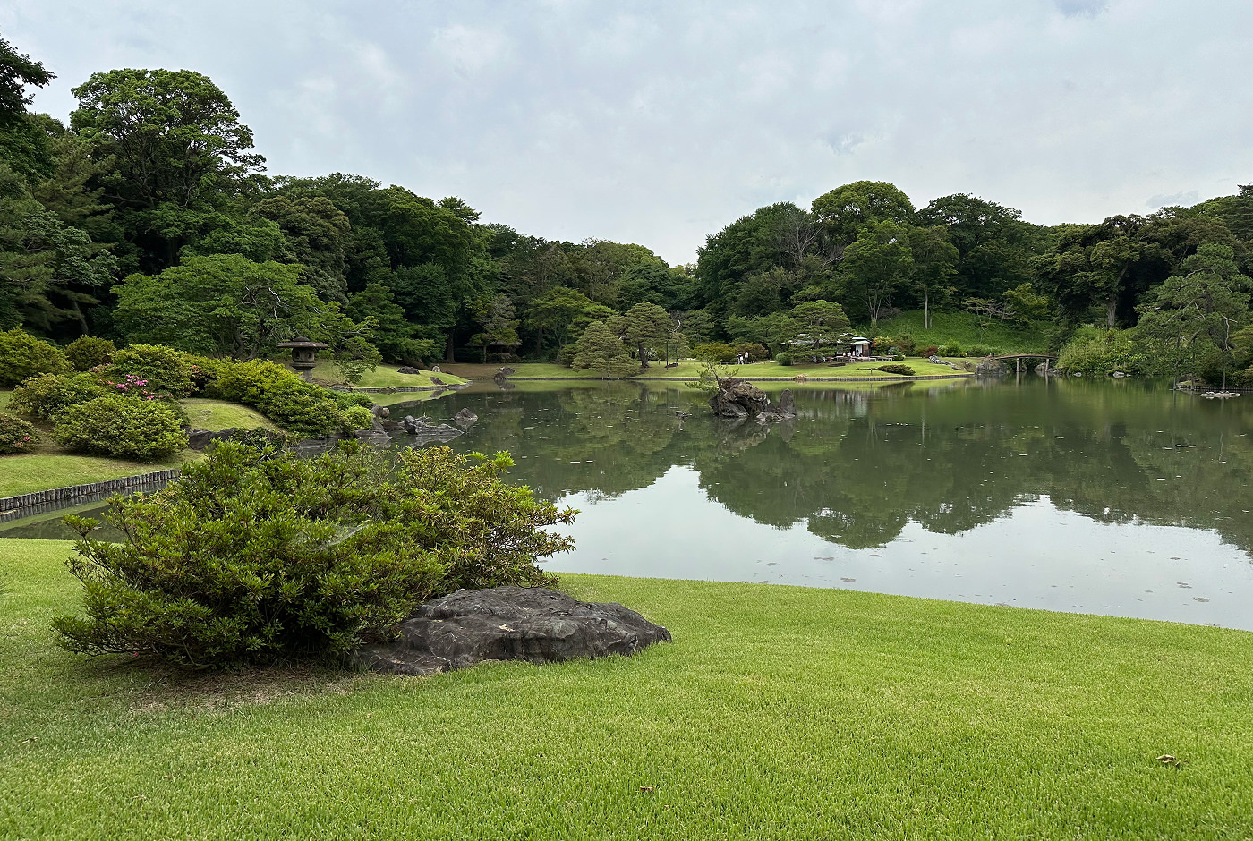 Traditionell japansk trädgård med en stor sjö i mitten omgiven av lummiga träd och buskar.