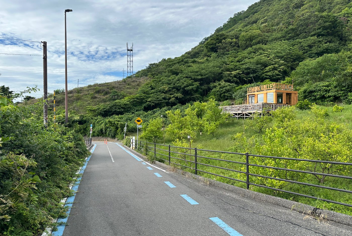Cykelväg ned för en backe i en lummig dal. En orange byggnad till höger har en skylt som lyder "Lemon Valley".