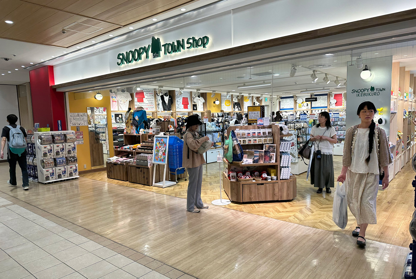 En ljus butik med många hyllor med kläder, kramdjur, kort, porslin med mera. Skylten ovan lyder "Snoopy Town Shop".