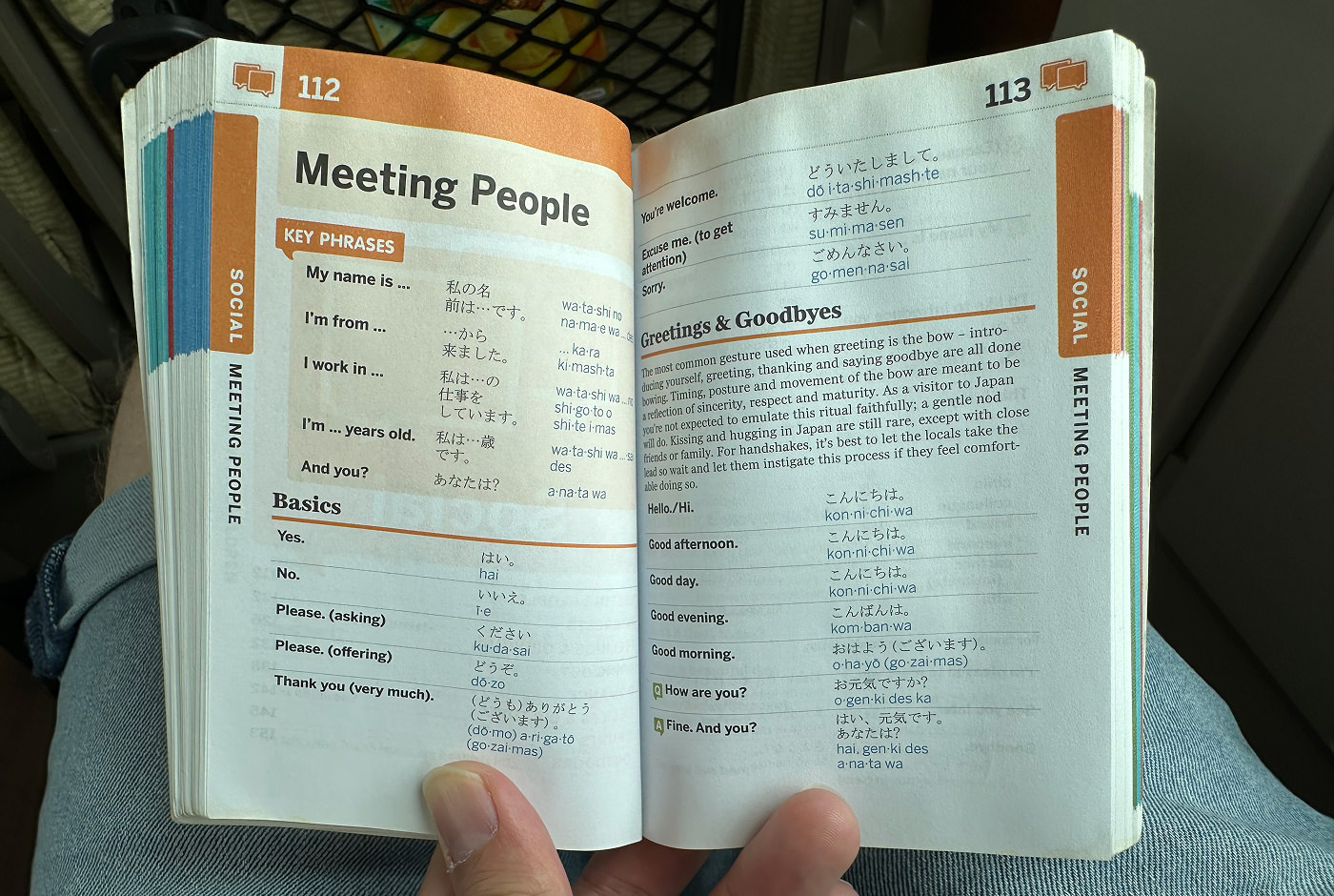 Hand håller upp en bok om japanska för turister. Kapitlet lyder "Meeting People".