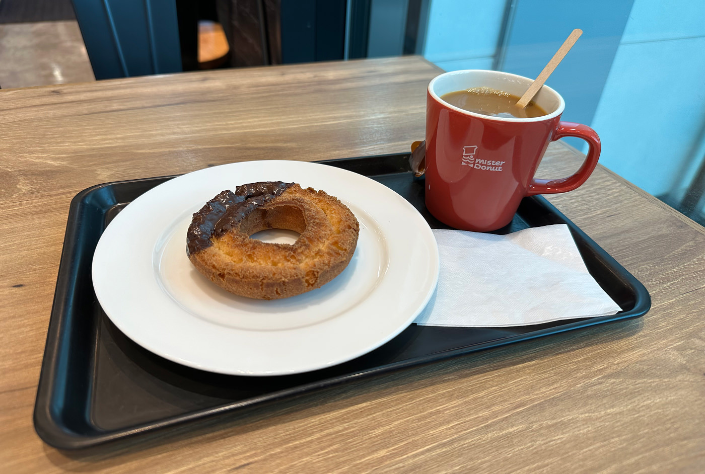 Svart bricka med en röd kopp med kaffe och en vit tallrik med en rund munk på.