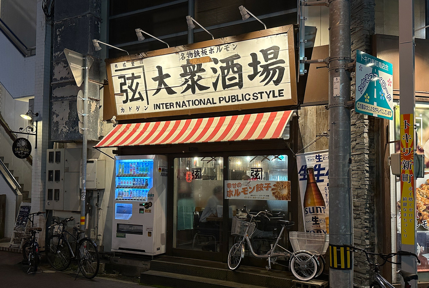 En liten bar med en stor vit skylt på japanska och undertexten "International public style". utanför står en läskautomat och en cykel.