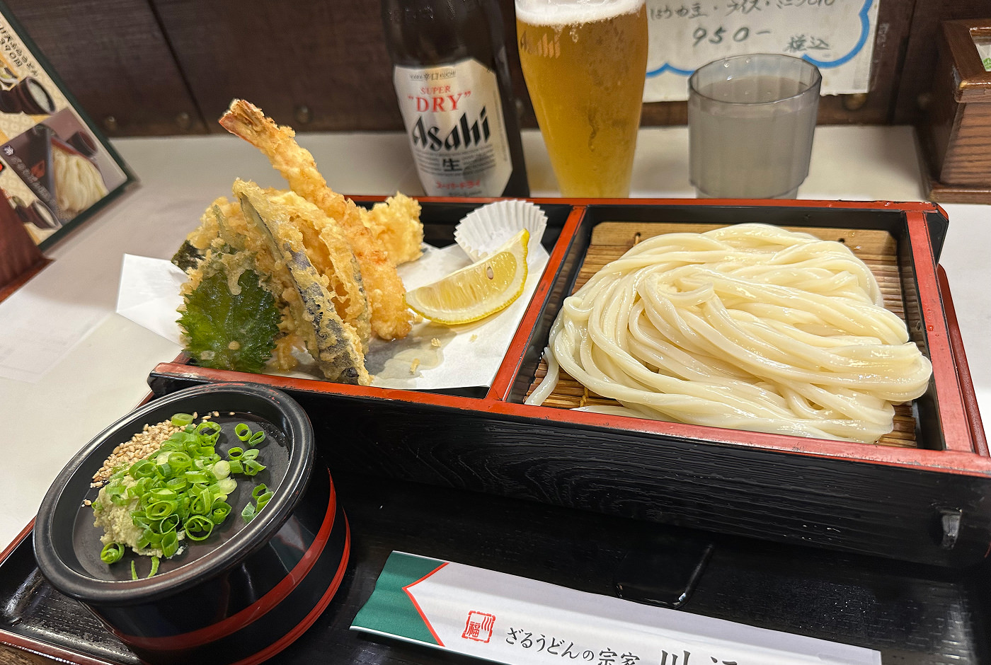 Matbricka med upphöjd låda med två fack. Det ena facket har några bitar tempura, det andra en klump nudlar.