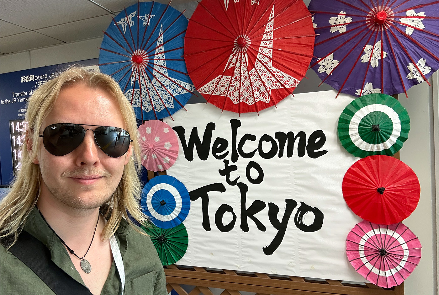 Jag stor vid en skylt med texten "Welcome to Tokyo". Jag har ett par solglasögon på och ler in i kameran.