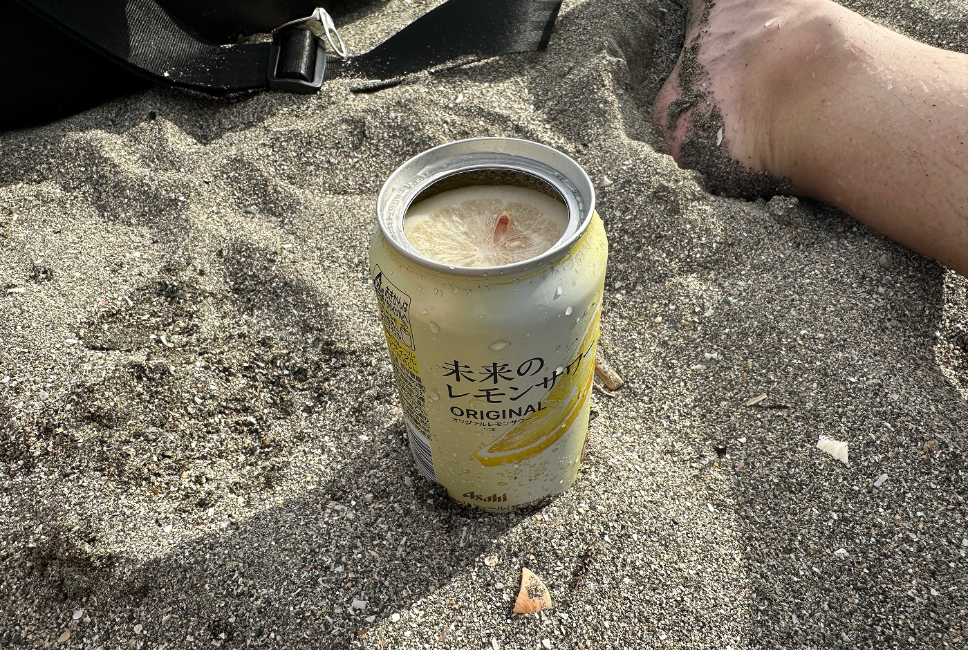 Ljusgul läskburk med en färsk citronskiva inuti står i sand.