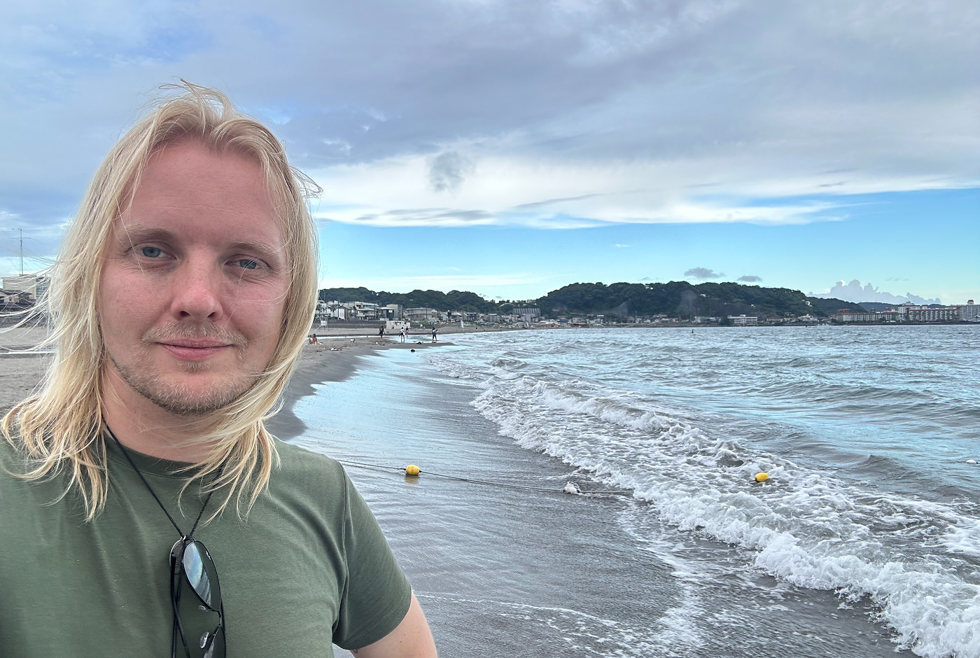 Jag står med vinden i håret vid en lång böjd sandstrand och ler in i kameran.