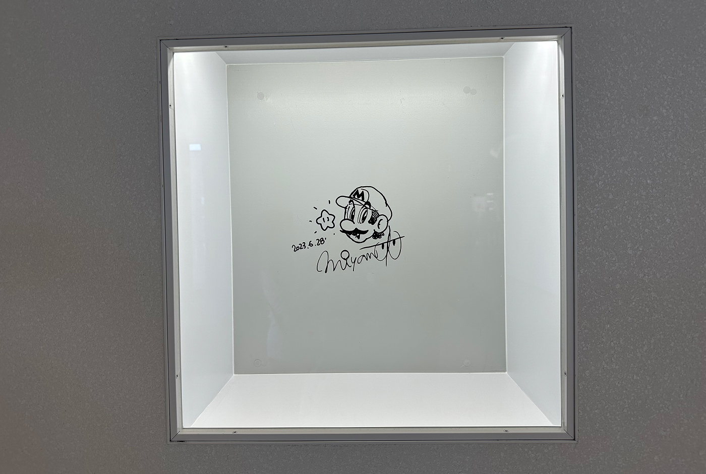 Upplyst liten vit monter med en teckning av Super Mario och en autograf av hans skapare Shigeru Miyamoto.