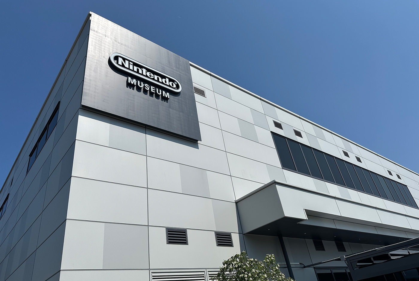 Modern grå byggnad med slät grå fasad i olika sektioner. En skylt lyder "Nintendo Museum".