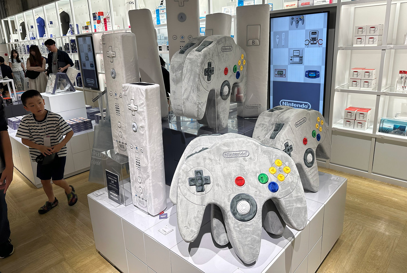 Tolv stora kuddar som föreställer kontroller till Nintendos konsoler Nintendo Wii och Nintendo 64. I bakgrunden finns upplysta hyllor med andra prylar.