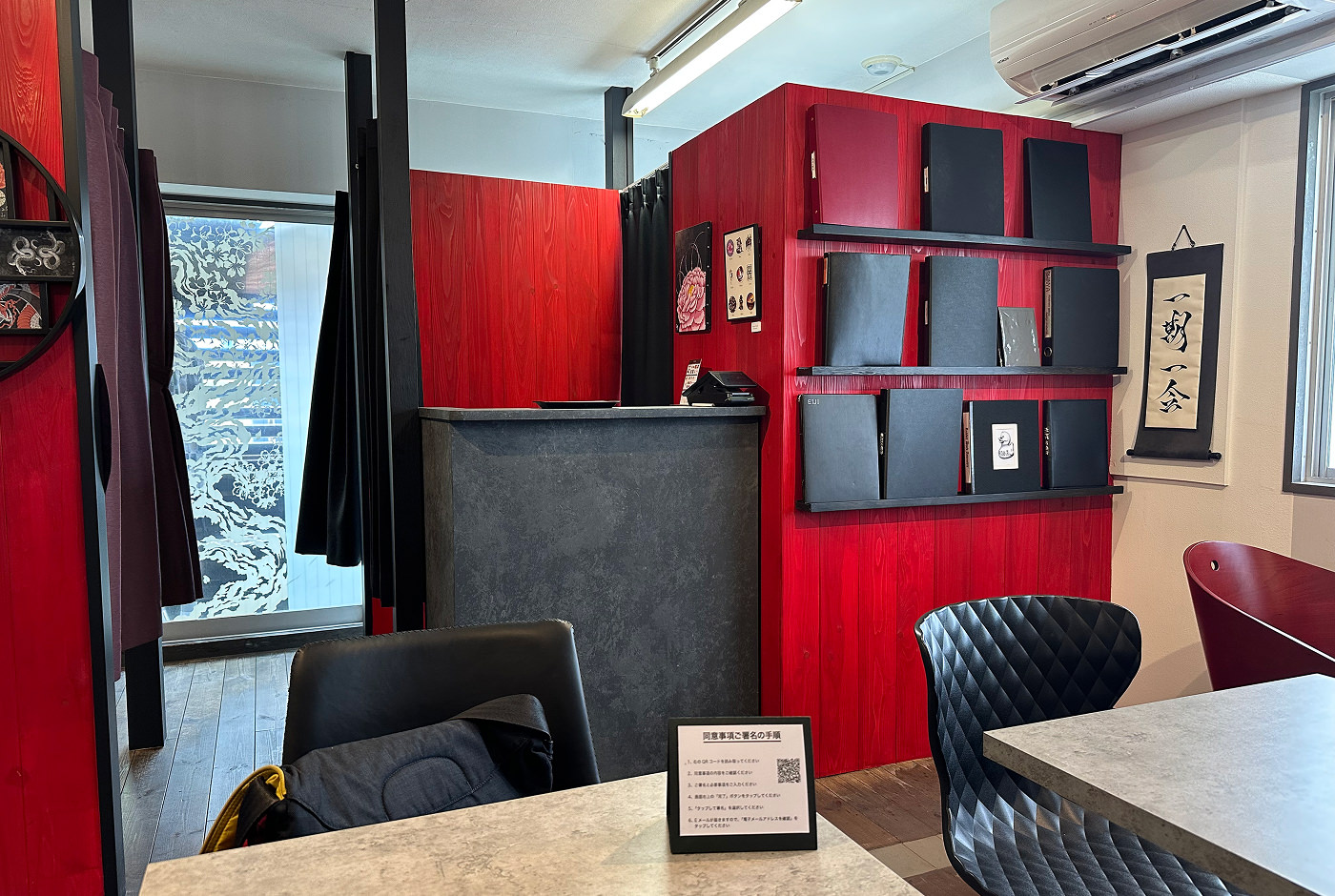 Lobby med några bord och en disk som ingen står bakom. Väggarna är vita, knallröda och på en hylla står det svarta pärmar.