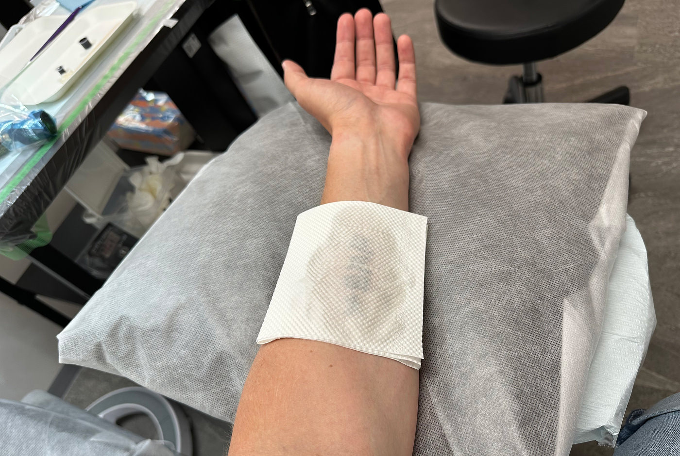 Min arm sträcker sig över en ljus kudde. Ett stycke böött papper täcker en tatuering på min underarm.