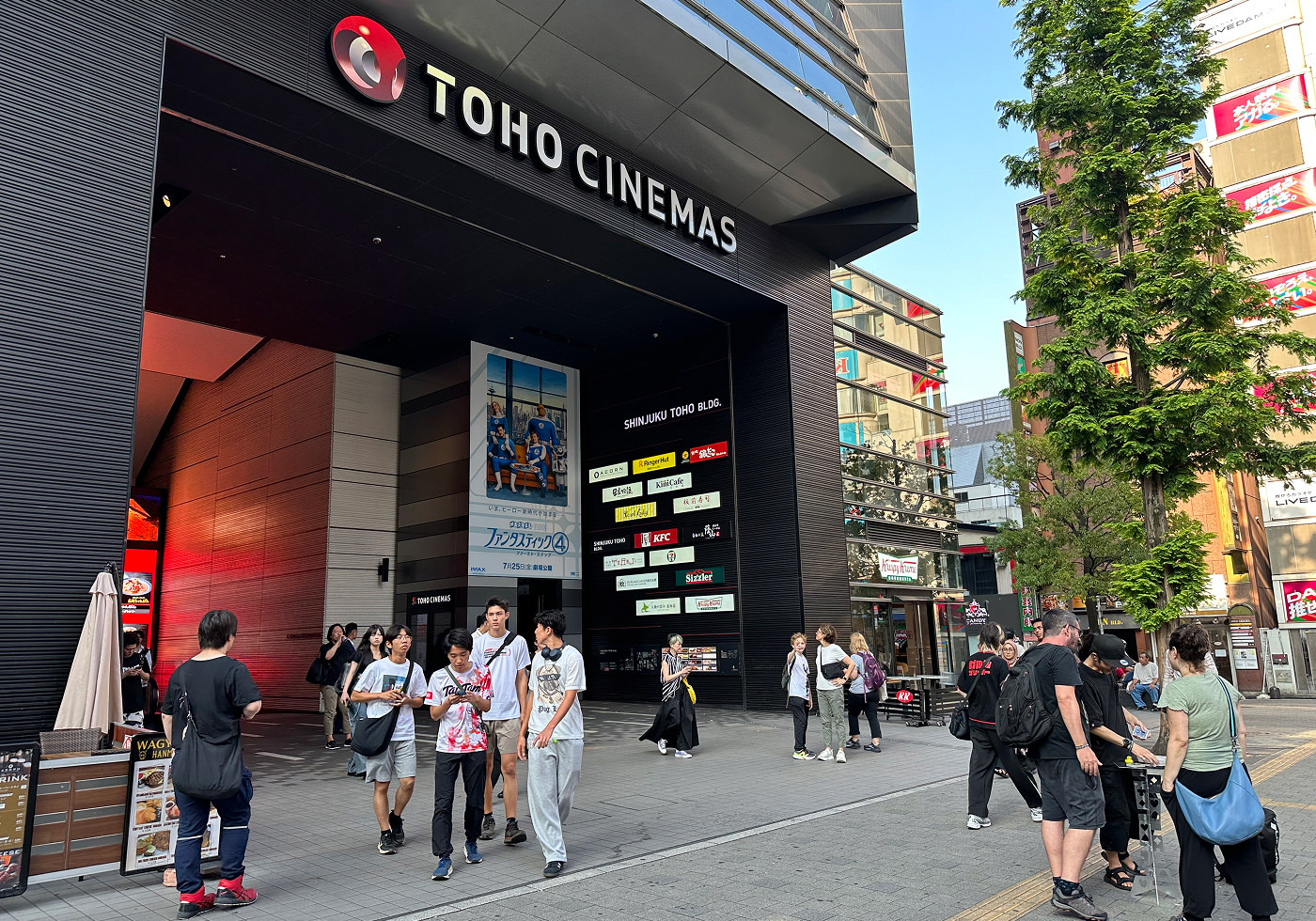 Enorm ingång till en svart byggnad med en vit skylt som lyder "Toho Cinemas". Utanför går ett trettiotal personer.