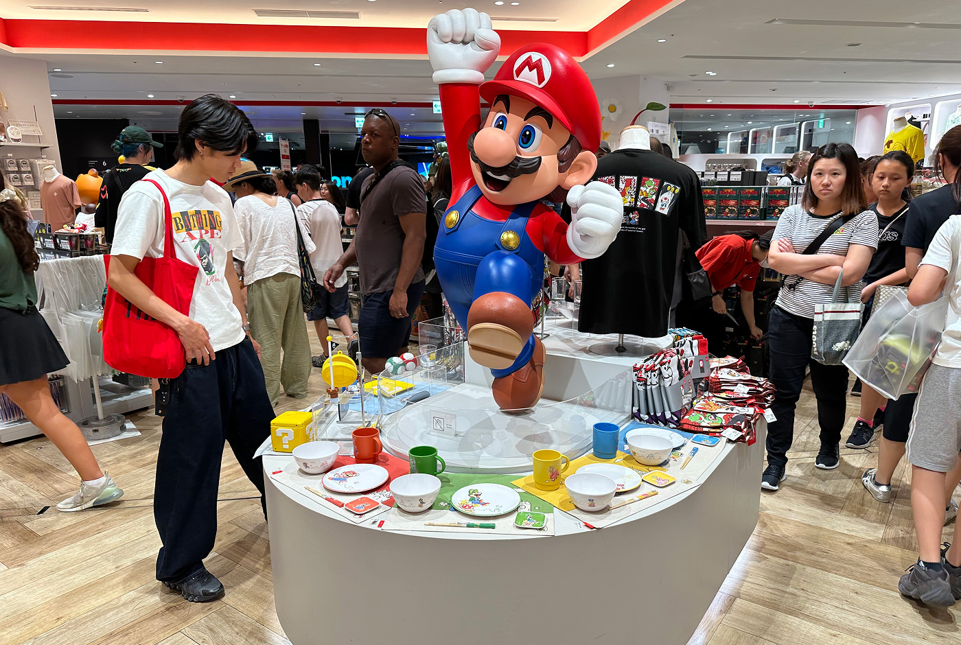En staty på Super Mario på ett bord inuti en butik. På bordet som är omgivet av besökare ligger det glas och tallrikar.