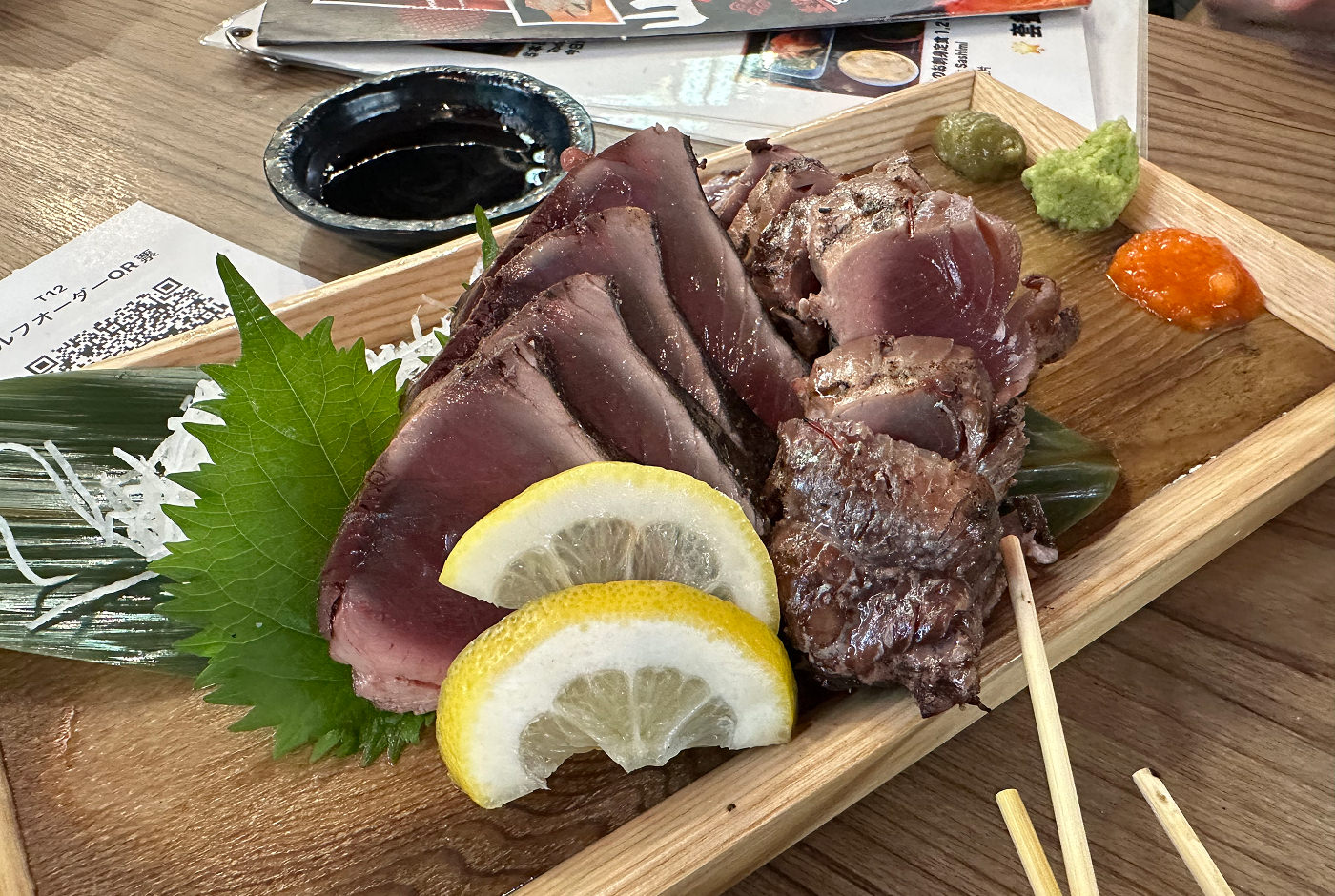 En träbricka med grillad och skivad tonfisk med lite sallad och citronklyftor.