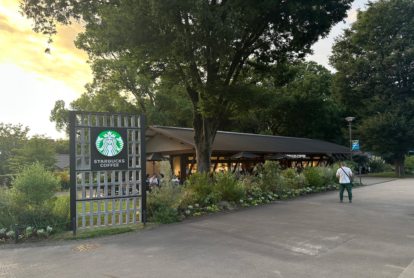 Stor och avlång Starbucks omgiven av buskiga träd i en park. En skylt utanför lyder "Starbucks Coffee".