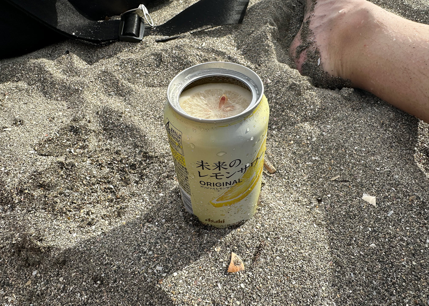 Ljusgul läskburk med en färsk citronskiva inuti står i sand.